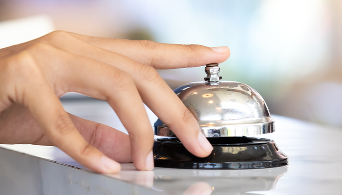 Close up of person's hand ringing front desk check in bell
